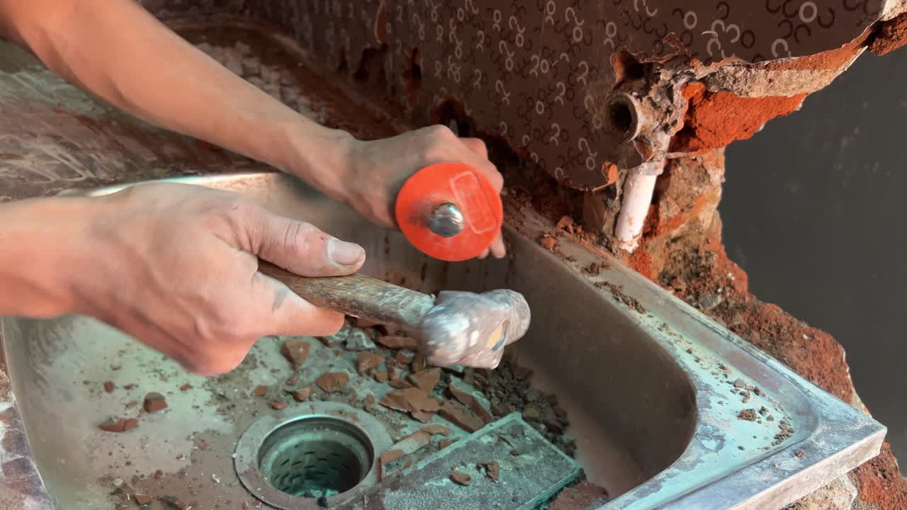 Kraftig nærbilde av mannshender som bryter ned en betongvegg manuelt med meisel for husrenovering