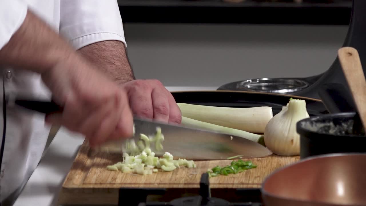 A chef skillfully prepares fresh vegetables in a modern kitchen. He demonstrates slicing leeks and onion, showcasing professional cooking techniques with precision and care