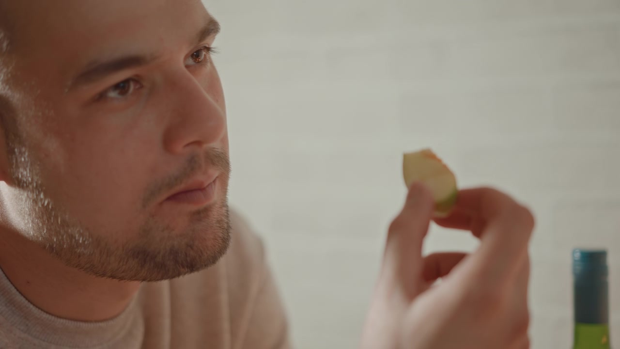 Medium close-up shows adult man in home kitchen lifting bite-sized snack toward lips with focused gaze, relaxed posture, and soft warm light, creating calm everyday food preparation mood