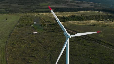 aerial arc shot around single wind turbine generator in grass field-1