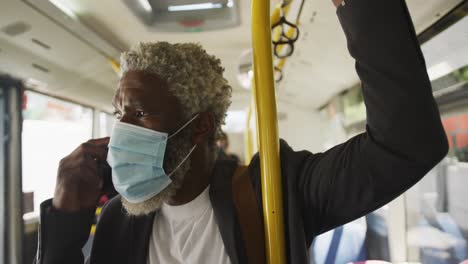 african american senior man wearing face mask talking on smartphone while standing in the bus