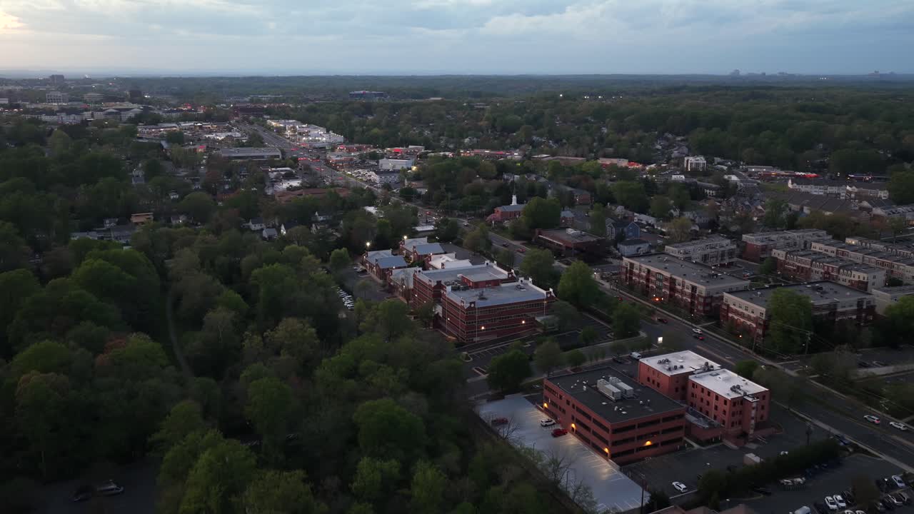 Aerial dusk flyover of Fairfax, Virginia showing Main Street lined with historic buildings, light traffic and tree-filled neighborhoods. Charming soft spring evening atmosphere in USA. Wide shot