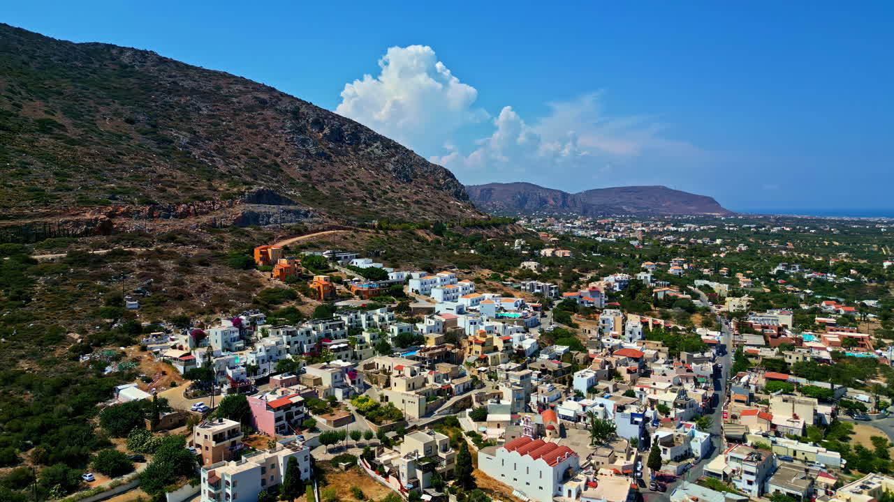 Piskopiano village in crete with colorful houses and hilly landscape under blue sky, aerial view