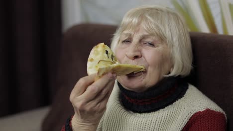 Beautiful-elderly-woman-is-sitting-on-sofa-and-eats-pizza