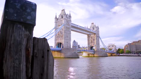 Looking-at-Tower-Bridge-in-London-on-a-sunny-summer-day-with-blue-sky-and-light-clouds,-wooden-pier