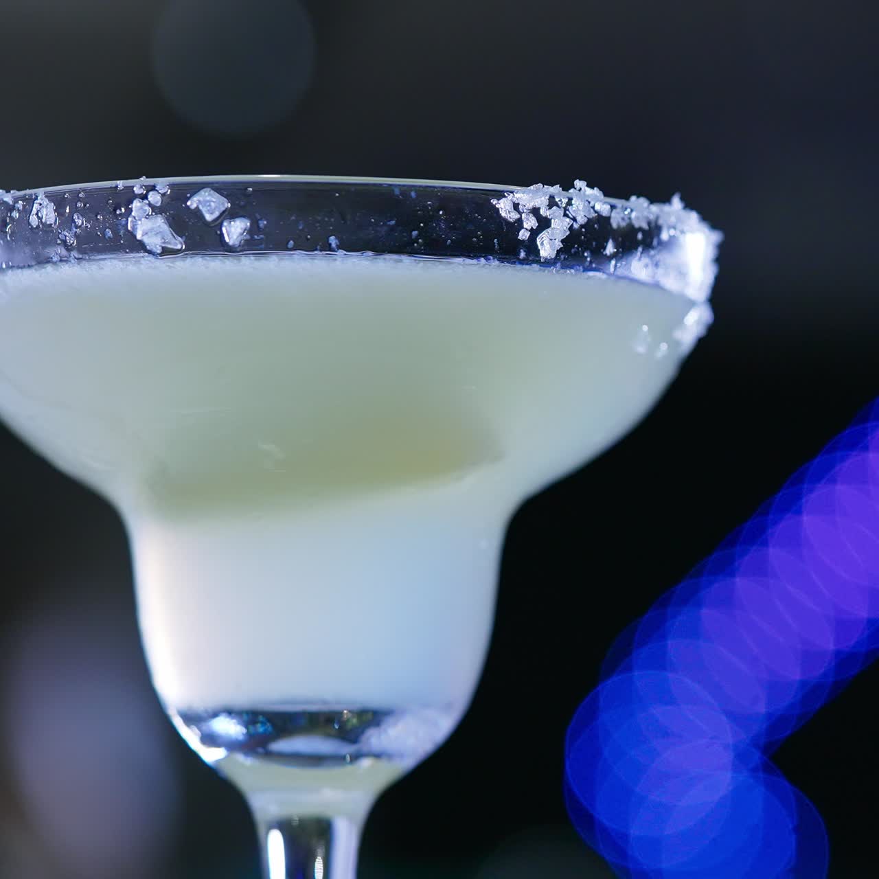 Margarita glass with white beverage. Glass top decorated with crystals of salt. Close up. Blurred backdrop