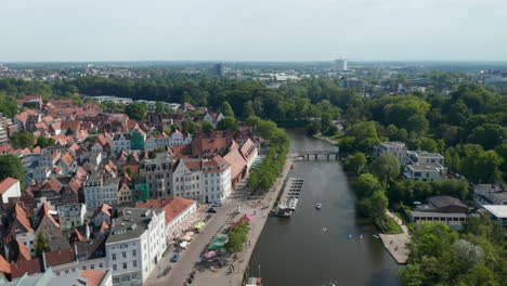 Aerial-view-sunshades-on-terraces-of-waterfront-restaurants.-Wide-street-along-Trave-river-and-historic-old-town.-Luebeck,-Schleswig-Holstein,-Germany