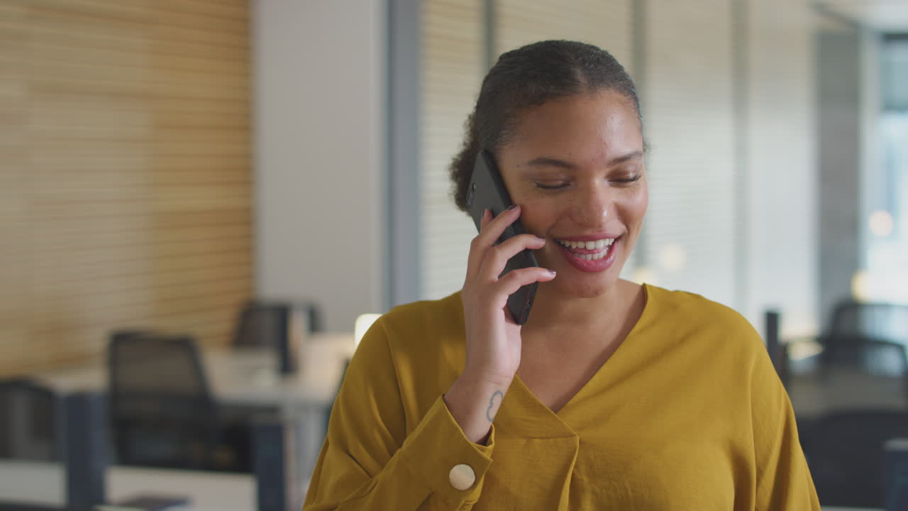 joven mujer de negocios sonriente en una llamada telefónica de pie en una oficina moderna de plan abierto