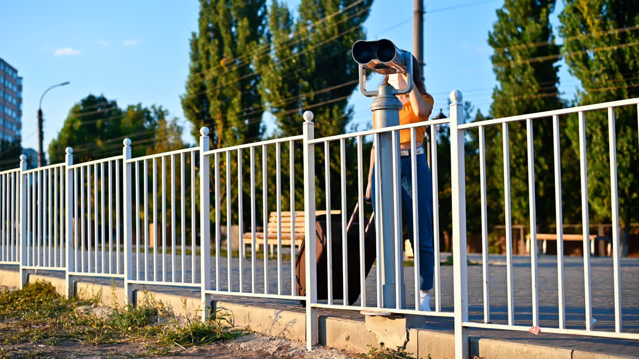 Young woman in protective medical mask looking into a tower viewer from the observation deck at the city at sunset. Corona Virus idea. Safe travel during the pandemic. Slow motion. Chisinau, Moldova