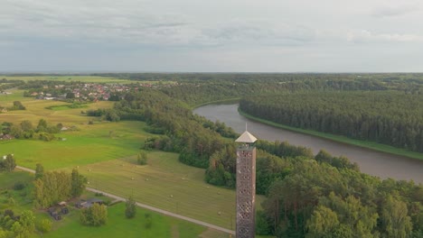 aerial view of wooden observation tower, river bend, lush green forest and village under cloudy summer sky in birstonas lithuania, orbit shot