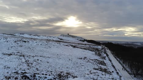 Snowy-Rivington-Pike-Tower-Winter-Hill-Vista-Aérea-Gente-En-Trineo-Cuesta-Abajo-Al-Amanecer-En-Ascenso