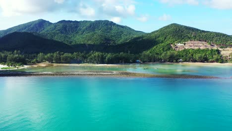 blue azure sea lagoon on beautiful shoreline of tropical island with white sandy beach and trees forest on hills in thailand