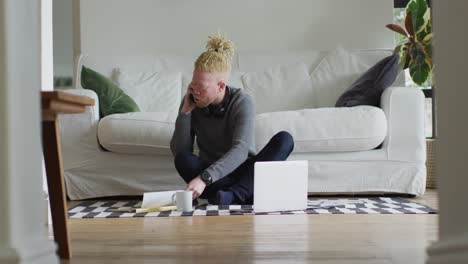 hombre albino afroamericano con rastas sentado en el suelo, trabajando y usando una computadora portátil