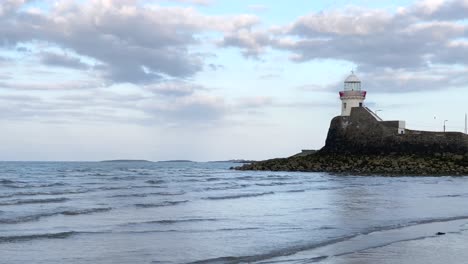 Winzige-Wellen,-Die-Den-Strand-Schlagen,-Mit-Dem-Im-Hintergrund-Sichtbaren-Schären-Leuchtturm