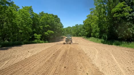 pov - siguiendo un tractor tirando de una harra a través de un campo para romper la tierra para nuevas semillas de cultivo en el medio oeste en un día soleado