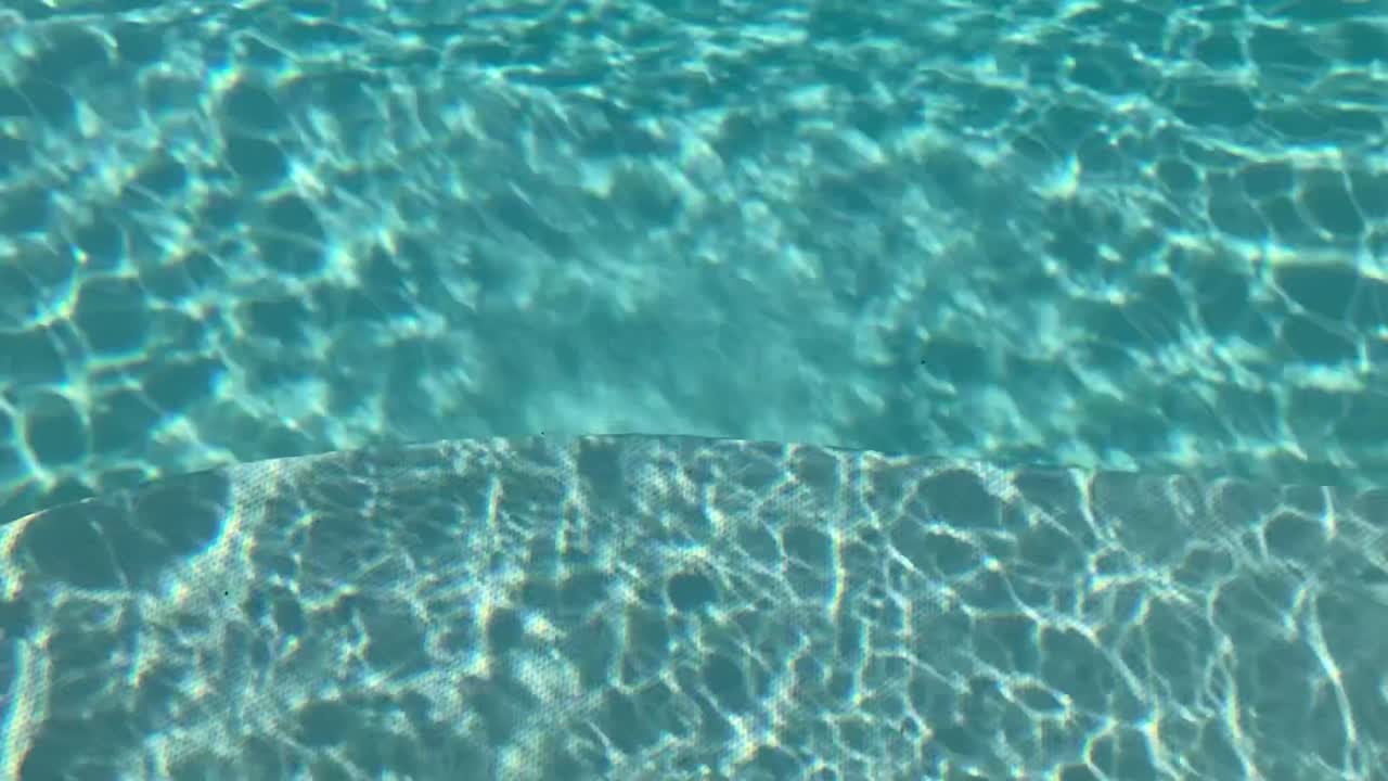 Sinar matahari berkilauan di air kolam renang yang beriak. Tekstur abstrak yang menangkap suasana musim panas, relaksasi, dan suasana liburan yang damai.