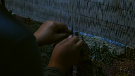 hands making carpet on loom