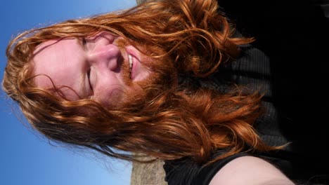 a long-haired man squints and smiles as he admires the beach