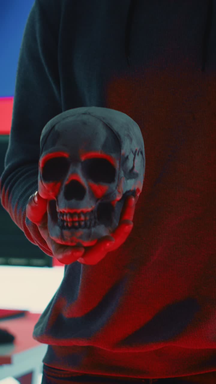 Mysterious Person in Hoodie Holding a Skull with Red Light