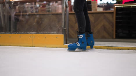 close-up of someone wearing blue skates and black trousers, gradually walking into an ice rink gradually