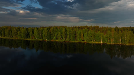 drone shot over a reflecting lake, toward polar woods, moody sunset in lapland