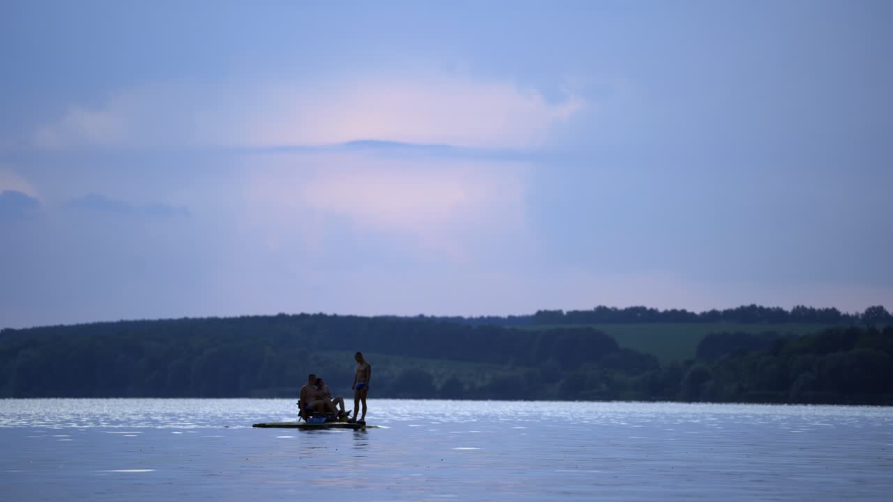 Three men sailing in a catamaran on the river in summer. Guys in swimming trunks only, floating in a pedal boat on a beautiful natural background in the evening.