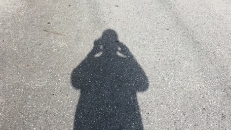 Man-Films-His-Shadow-Walking-Along-An-Asphalt-Road-With-His-Phone