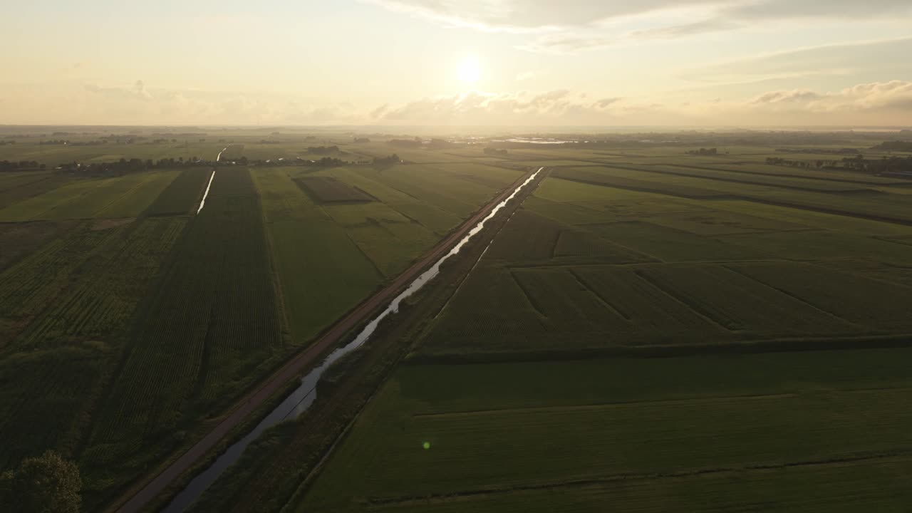 Drone aerial view above green farmland with dramatic sunset clouds and warm orange light