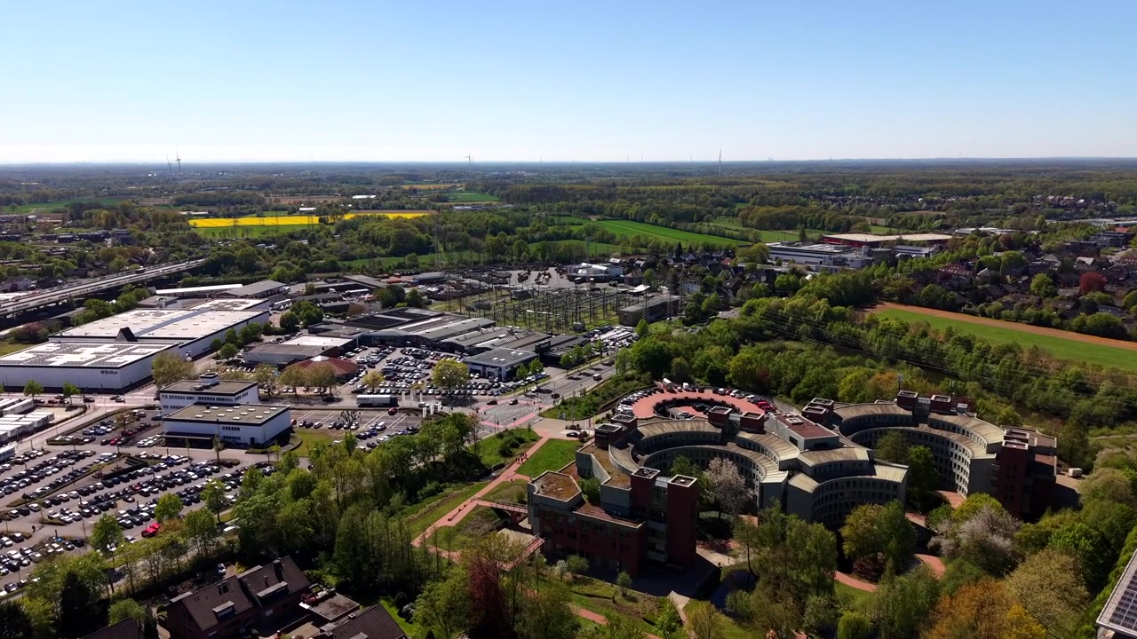 Naturskøn luftoptagelse af et virksomhedscampus om foråret med kontorer, parkeringspladser og omkringliggende træer, med gule rapsmarker og klar himmel i baggrunden i et levende forstadsmiljø. Amerikansk by, USA.