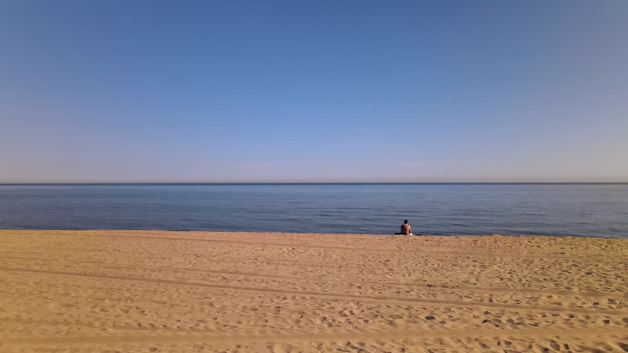 Static shot of beach with man staring at the ocean