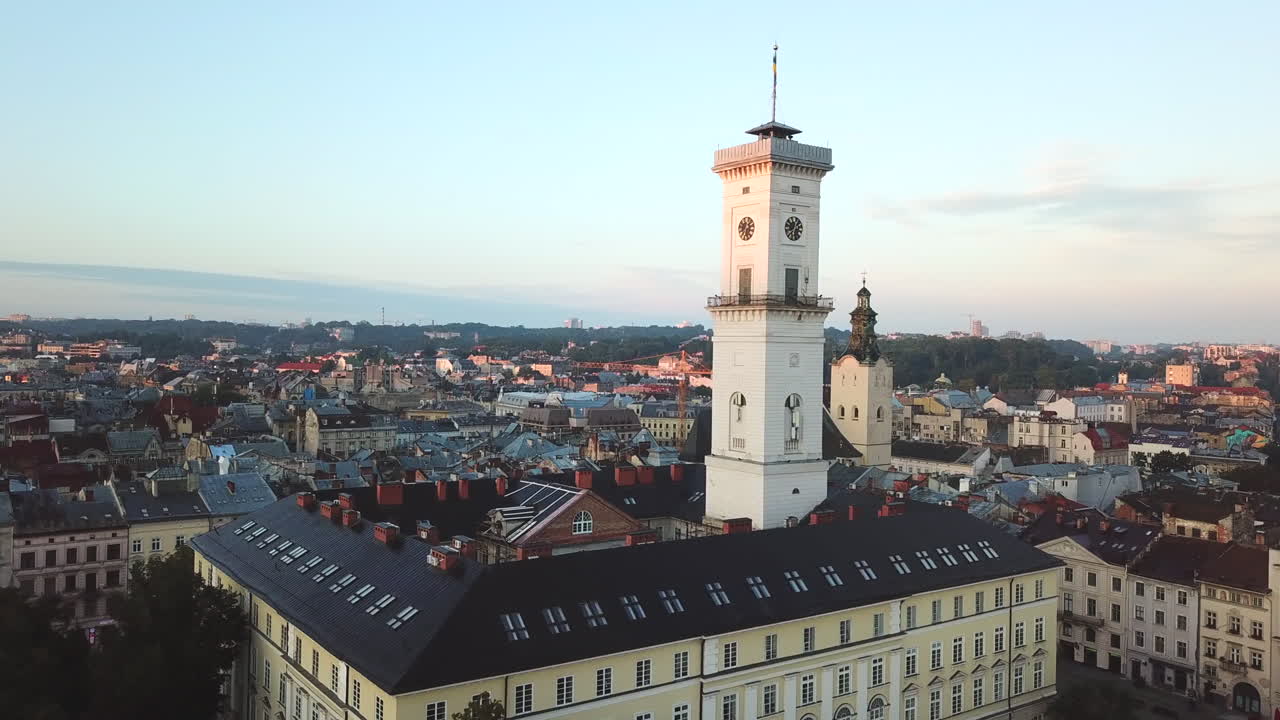 Ukraine,Lviv,City Hall,Clock Tower at Rynok Square during sunset, drone footage zooming in to the clock tower,a bird flies by, horizontal city view with pinkish clouds at the ground.