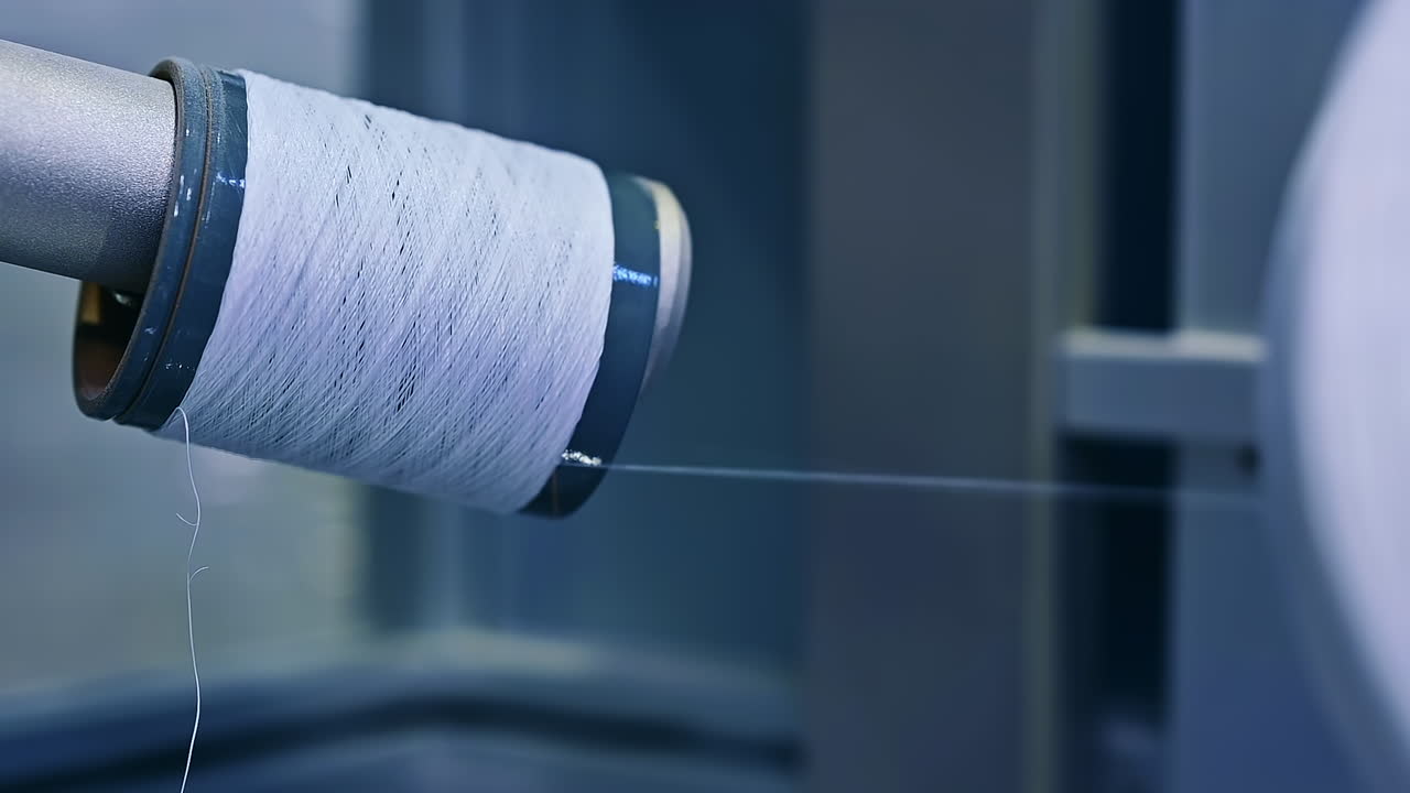Nylon white thread being unwind from a thick reel. Thread used for sewing the diaper parts at the nappies factory. Close up.