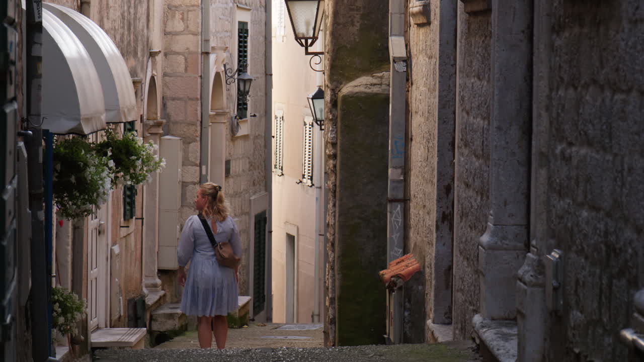 Blonde in dress walk in idyllic narrow old town street in Herceg Novi Montenegro