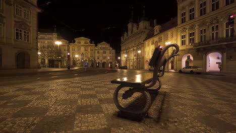 a bench on the empty malostranské square with a tram stop and rails in the historical centre of prague, czechia, at night lit by street lights, during a covid-19 lockdown with no people anywhere
