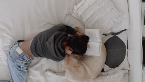 Woman reading a book and relaxing at home with her dog. Adorable moment between owner and her pet. Cozy, peaceful atmosphere showing the bond between owner and dog at home. Woman kisses her labrador