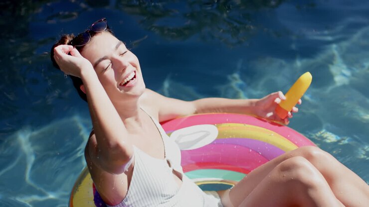 Teenage Caucasian girl enjoys the sun on a colorful float in a pool, holding a popsicle