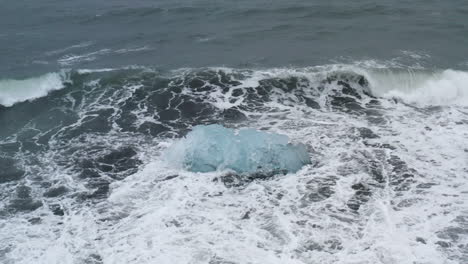 Atemberaubende-Drohnenaufnahme-Von-Wellen,-Die-Auf-Einem-Wunderschönen-Eisfelsen-Am-Diamond-Beach-In-Island-Brechen