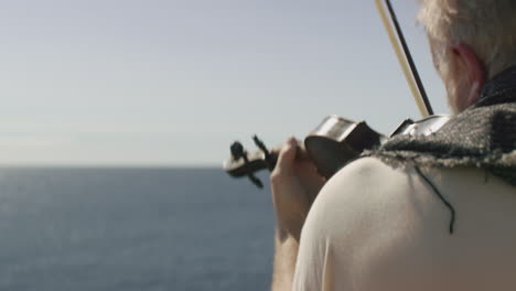 a man is playing the violin while looking out at the sea