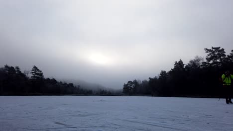 Timelapse-Of-Ice-Skaters-Skating-On-Frozen-Lake-With-Dramatic-Clouds,-Winter-Landscape