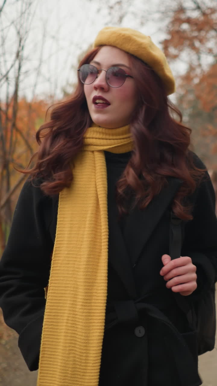 은 곱슬머리를 가진 여인이 가을 잎자루로 숲길을 걸어 웃으며 검은 가방을 들고 두 사람이 반대 방향으로 지나갈 때