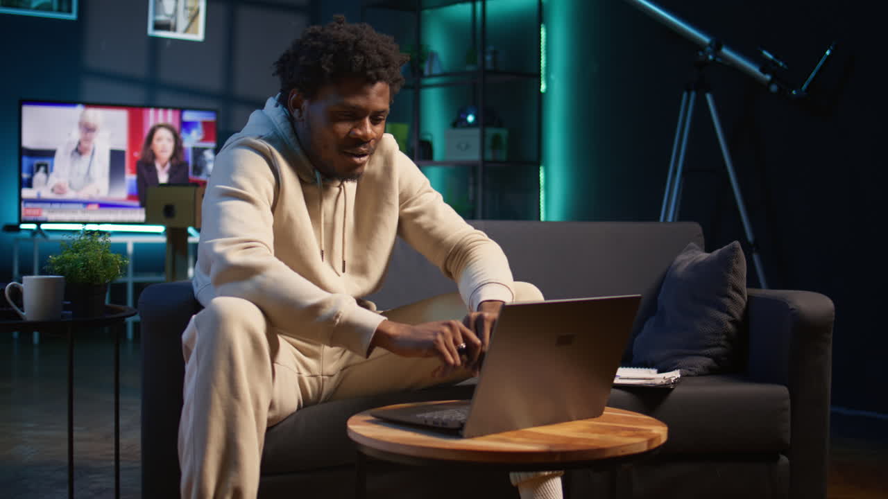 Confident young man solving daily tasks on a freelance platform at home, answering emails and multitasking. Person staying connected and enjoying the flexibility of working remotely. Camera B.
