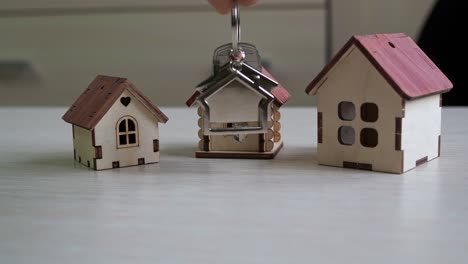 llavero con las llaves del nuevo apartamento en la mano. casas de juguete de madera contrachapada en la mesa. compra de bienes raíces