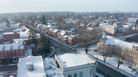 winter establishing shot of snow-covered homes and businesses in small town square as traffic passes by