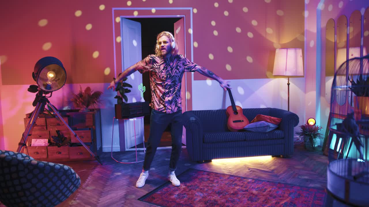 Young stylish caucasian man with long hair in glasses and headphones dancing energetically in a retro party at home