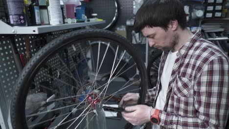 technician adjusts bicycle spokes and repairs wheel in bike store workshop. mechanic adjusts bike spokes and repair wheel. a velomechanic at work, checks tension of the spoke with a special tool.