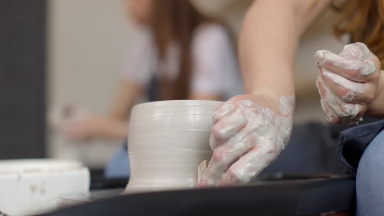 Mujer joven en estudio de cerámica usando torno de alfarero, cerámica hecha a mano, creativa. Primer plano de las manos, cámara lenta
