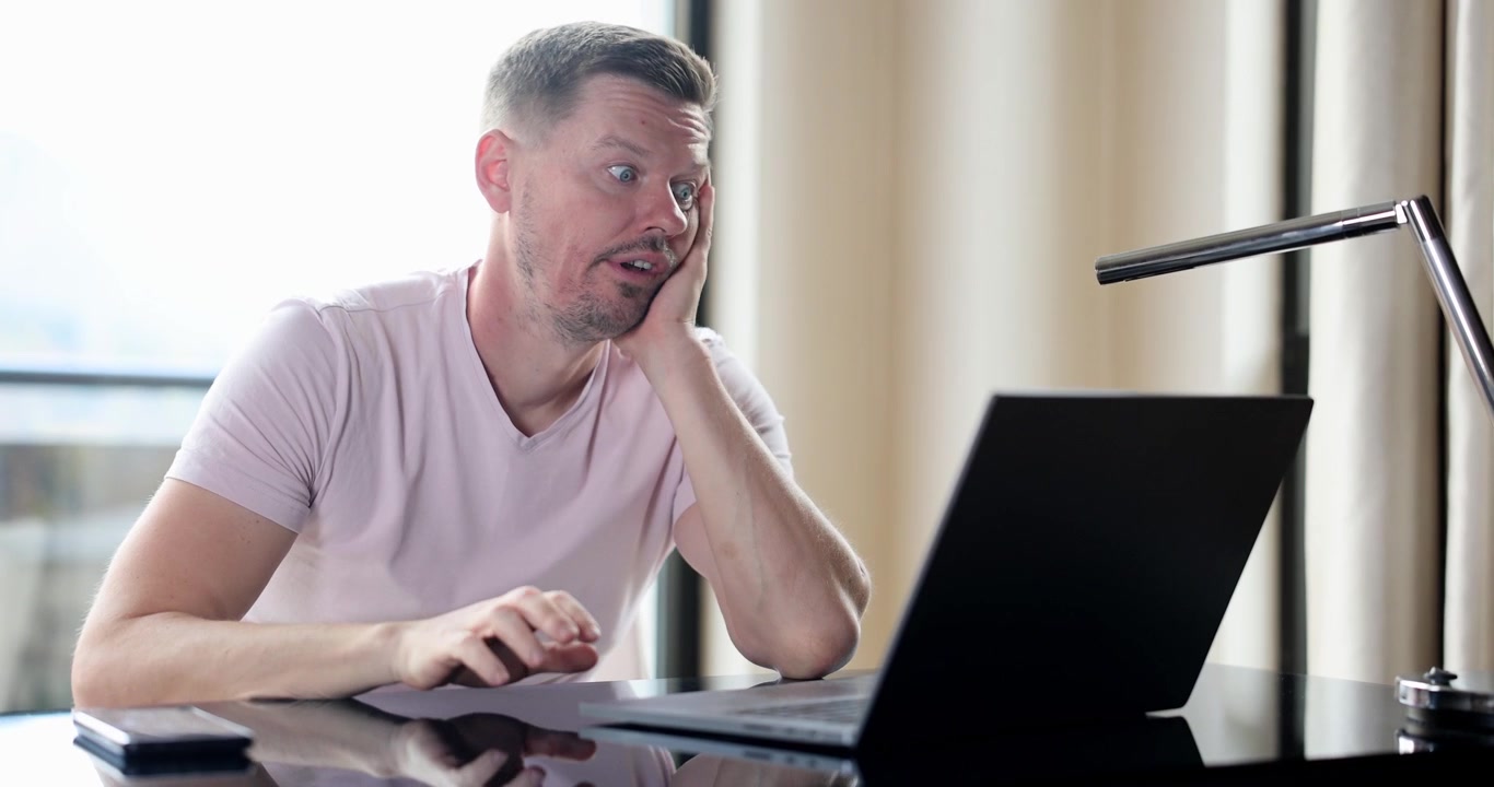 Businessman taps desk switching hands and resting chin at laptop