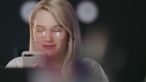 una mujer de negocios sonriente escribiendo un mensaje en su teléfono inteligente en la oficina nocturna.