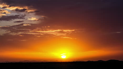 timelapse view of golden orange sun rays flowing out through cloudscape over silhouetted landscape