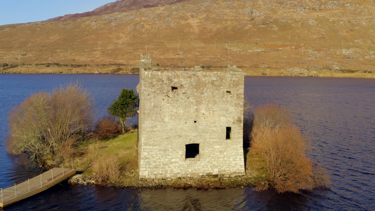 Establishing shot of O'Flaherty Castle as the drone tilts down from Benlettery Mountain, revealing the castle on Ballynahinch Lake, Connemara, Galway, Ireland.
